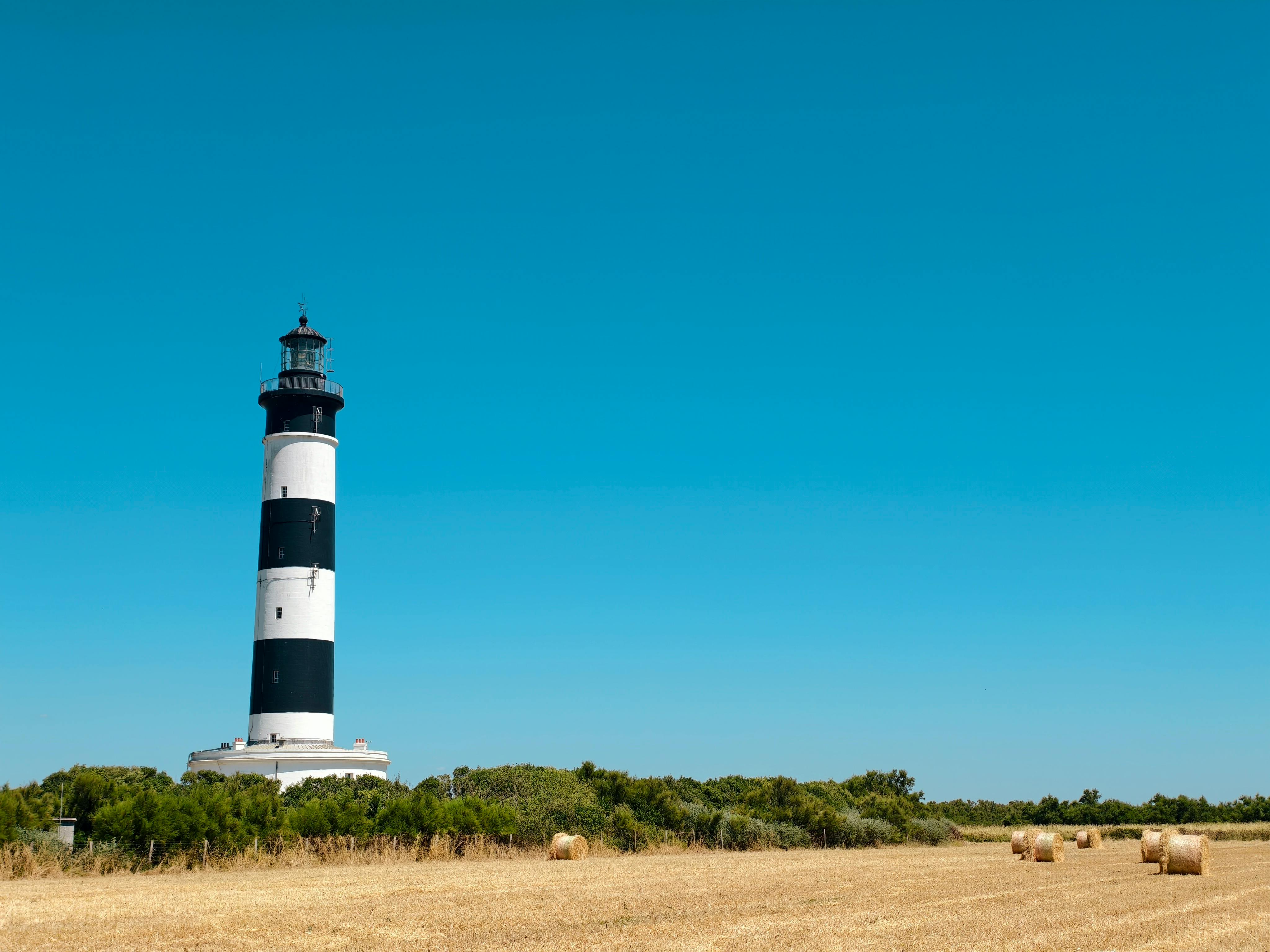 Captivating view of Chassiron Lighthouse with hay bales under a clear blue sky in Saint-Denis-d'Oléron.