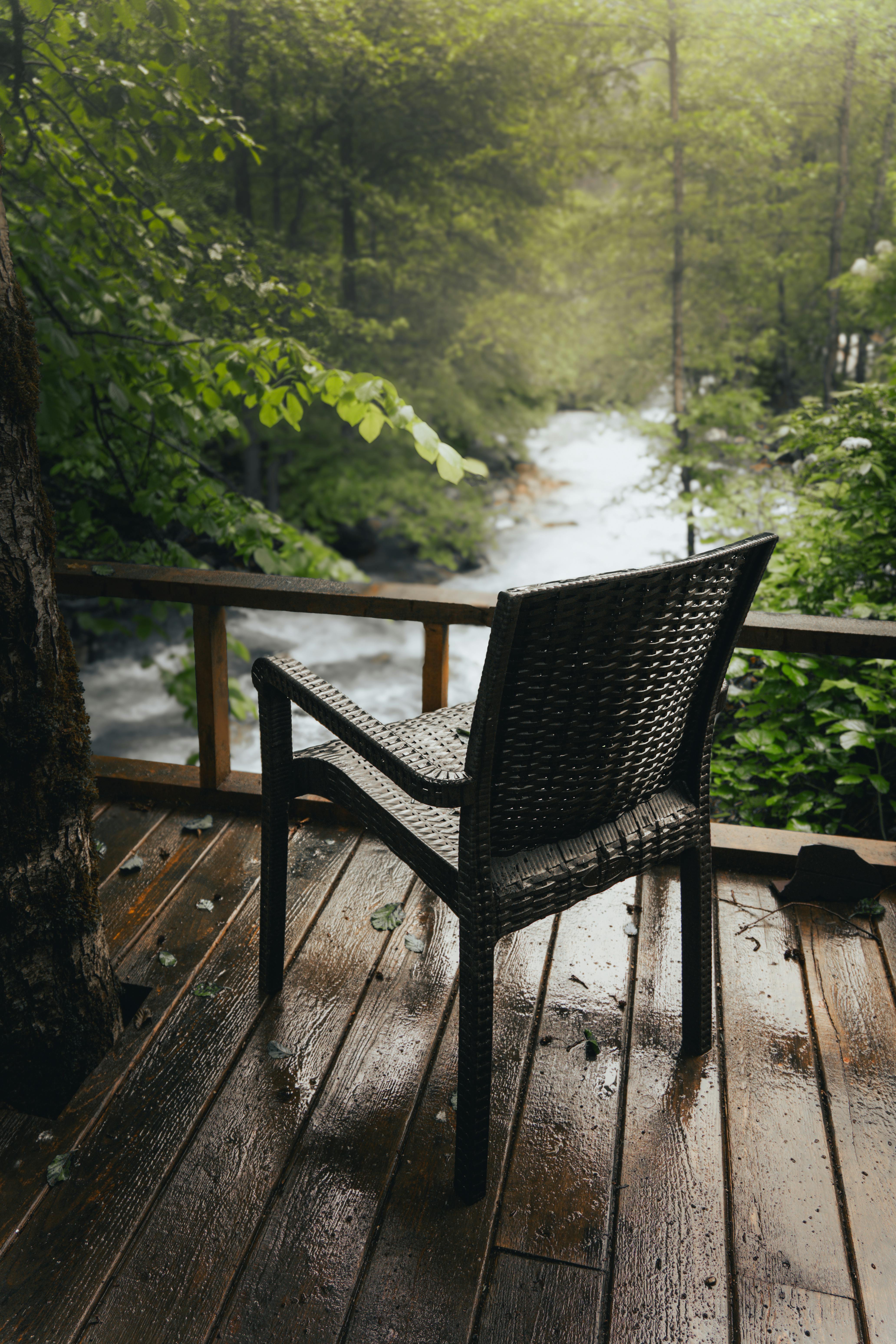 A solitary chair on a wooden deck overlooks a lush, green forest and flowing river.