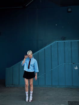 A fashionable individual poses outdoors in front of a blue wall in Istanbul, Türkiye.
