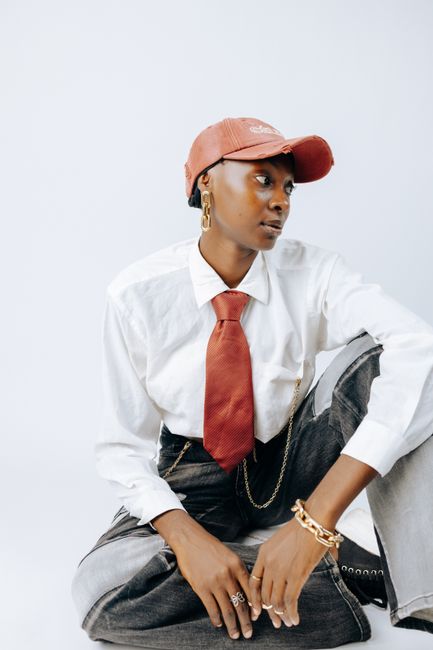 Fashionable woman in cap and tie with a unique style sitting in a bright studio.
