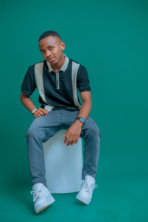 Free Portrait of a young man in casual attire sitting against a solid teal background. Stock Photo