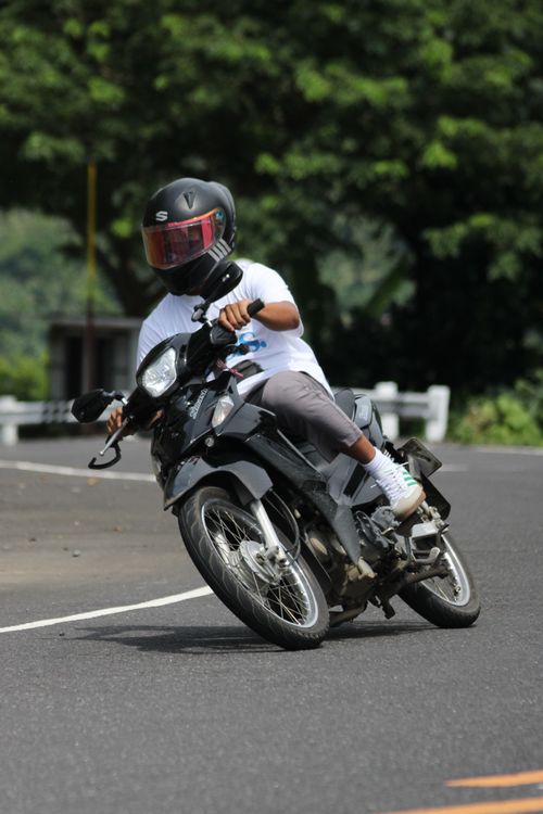 Free Motorcyclist wearing helmet leans into a turn on a winding road, showcasing dynamic motion and skill. Stock Photo