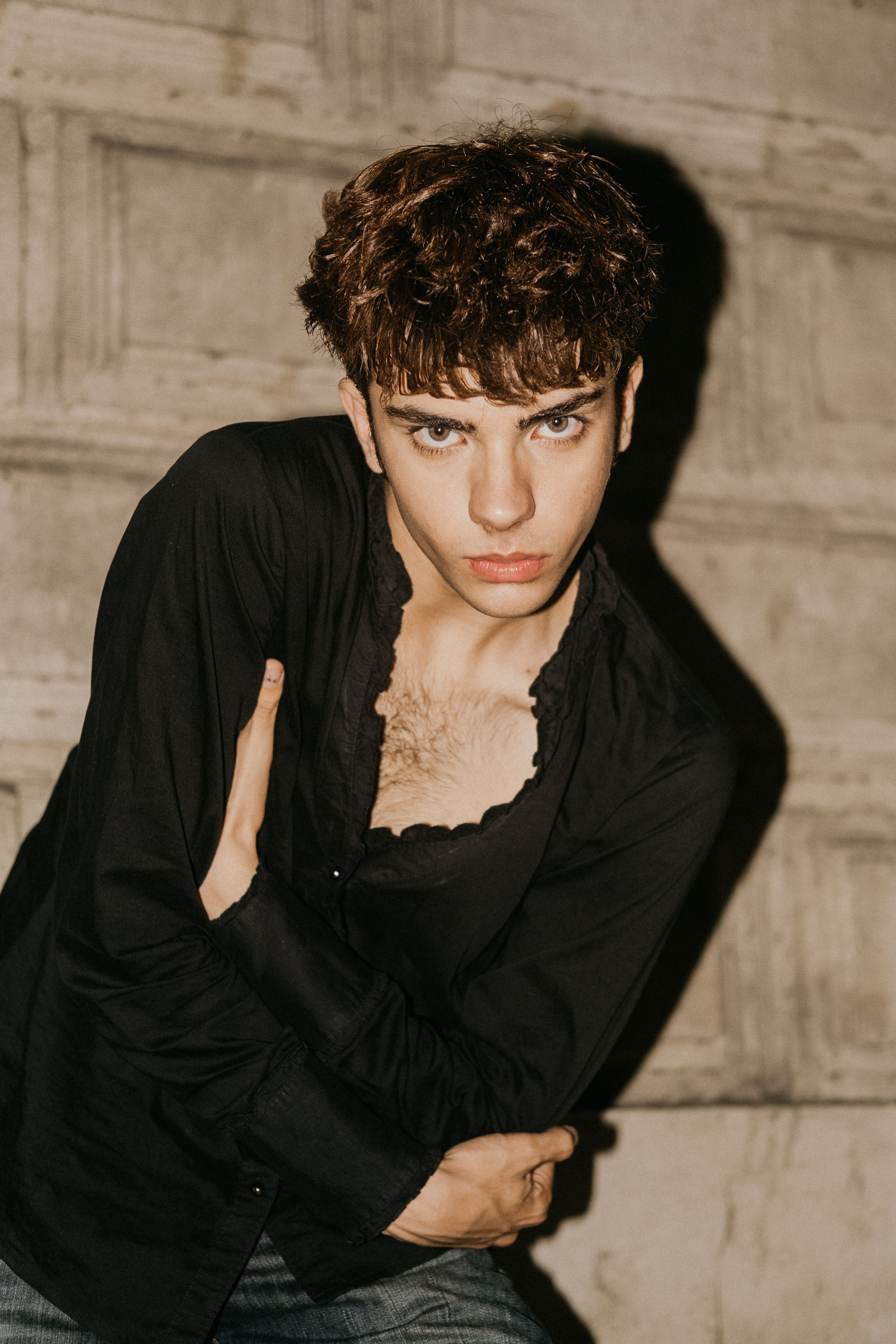 Portrait of a young man with striking features, wearing a black shirt, posing confidently outdoors.