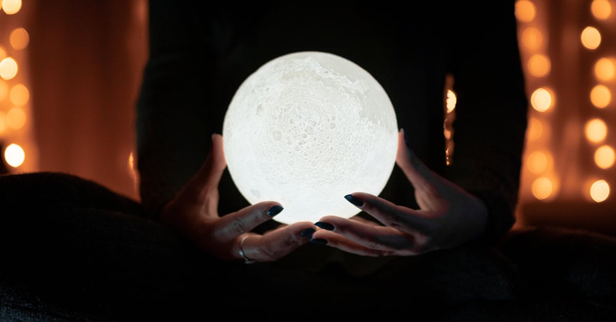 A person holding a glowing moon lamp, surrounded by warm bokeh lights, creating a mystical indoor atmosphere.