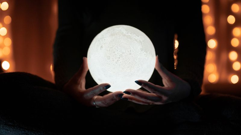 A person holding a glowing moon lamp surrounded by warm bokeh lights
