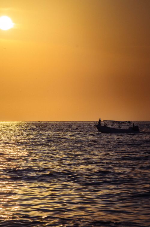 Free A serene sunset over Sayulita, Mexico with a fishing boat silhouette on sunlit waters. Stock Photo