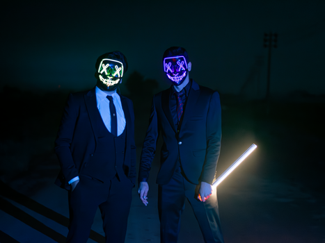 Two men wearing LED masks and suits stand outdoors at night, emitting a mysterious vibe.