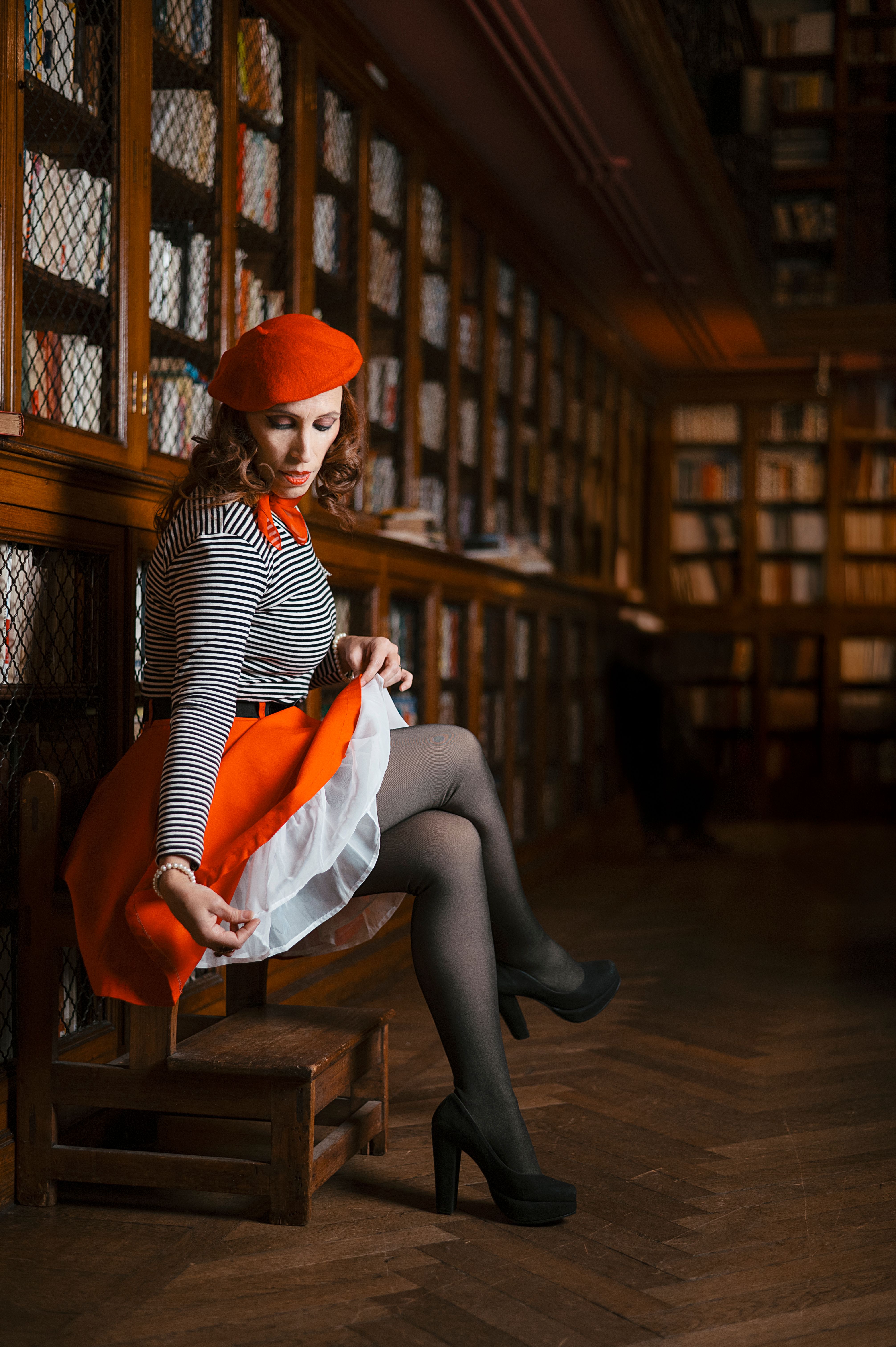 Gratis Donna chic in un abito vivace che posa elegantemente in una classica biblioteca. Perfetta per temi di moda e letteratura. Foto a disposizione