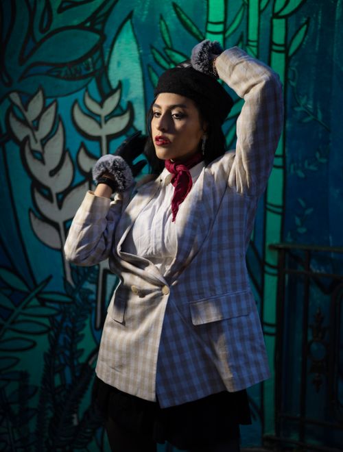 Free Chic woman in a plaid blazer and beret poses confidently against an urban mural backdrop. Stock Photo