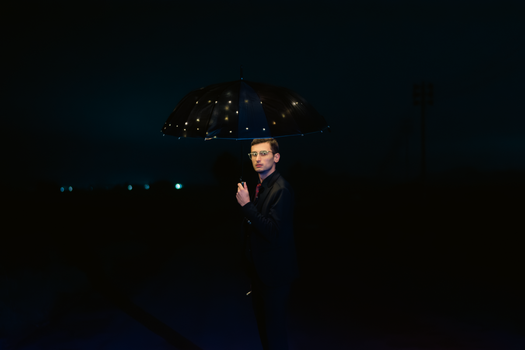 Elegant nighttime portrait of a man holding an illuminated umbrella, exuding charm and style.