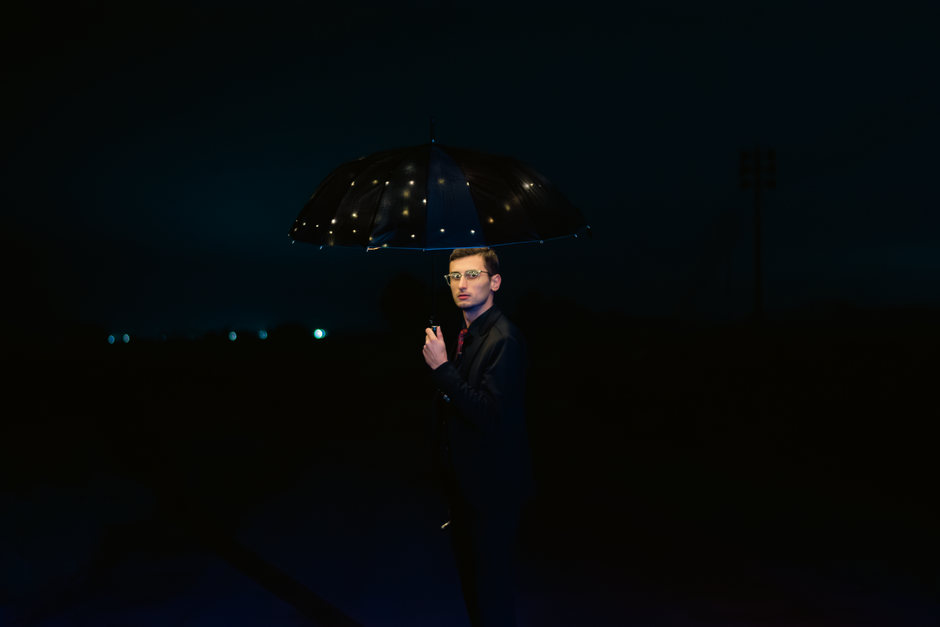 Elegant nighttime portrait of a man holding an illuminated umbrella, exuding charm and style.
