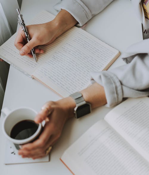 Persona Escribiendo En El Cuaderno Mientras Sostiene La Taza De Café