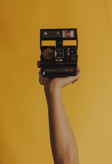 A person's hand holding a vintage Polaroid camera against a vibrant yellow background.