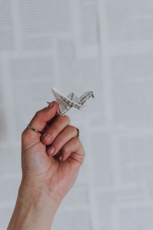 Free Close-up of a hand holding a paper origami crane made from newspaper. Stock Photo