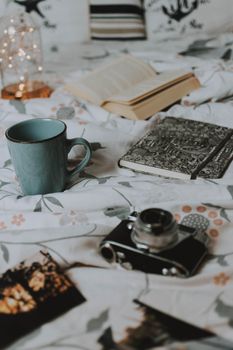 Warm, cozy setting with coffee mug, vintage camera, and open book on bed.