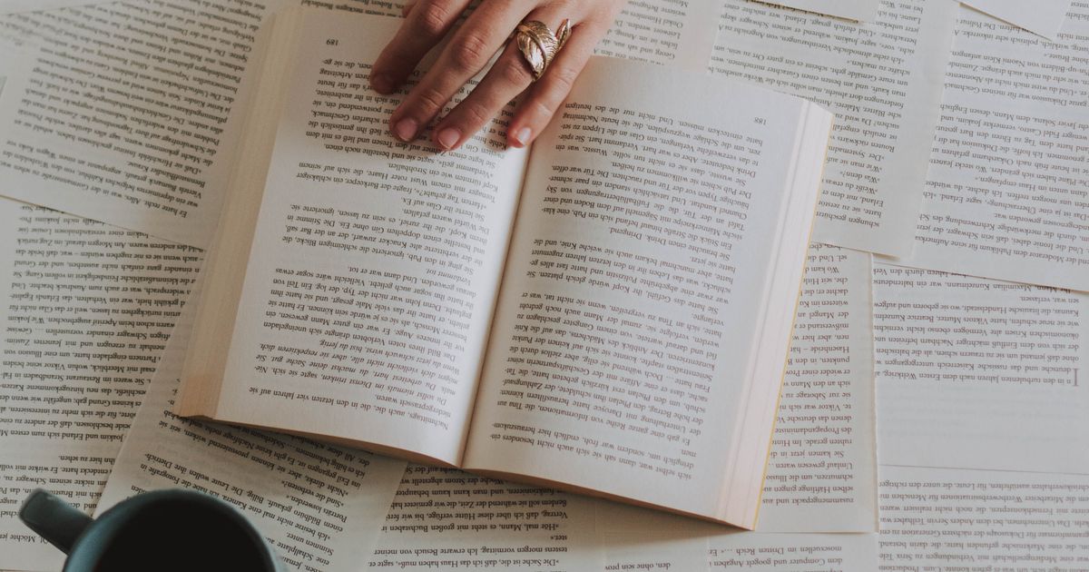 Open book with a hand resting on the page next to a coffee mug