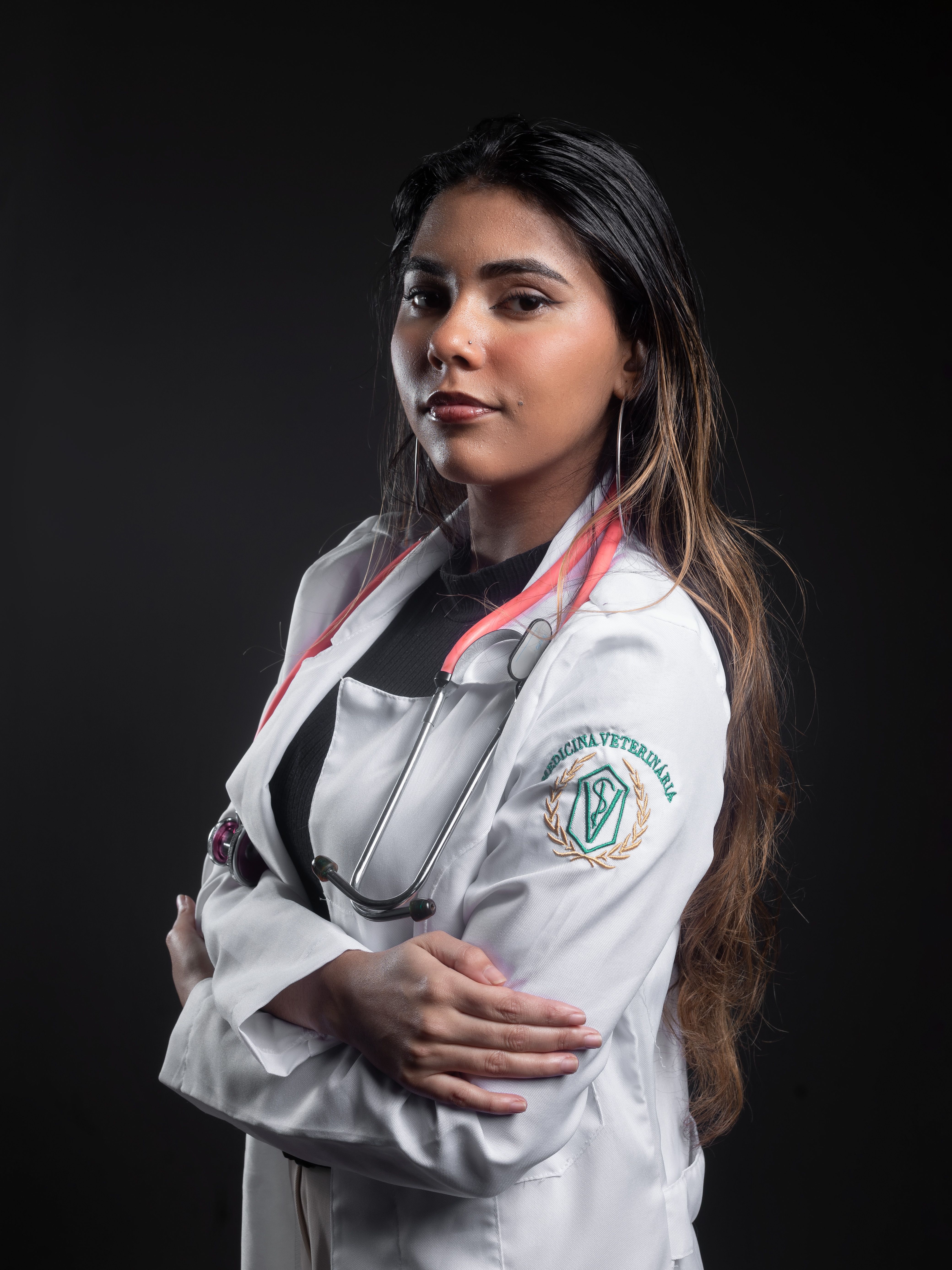 Portrait of a confident female veterinarian in a lab coat with a stethoscope, dark background.
