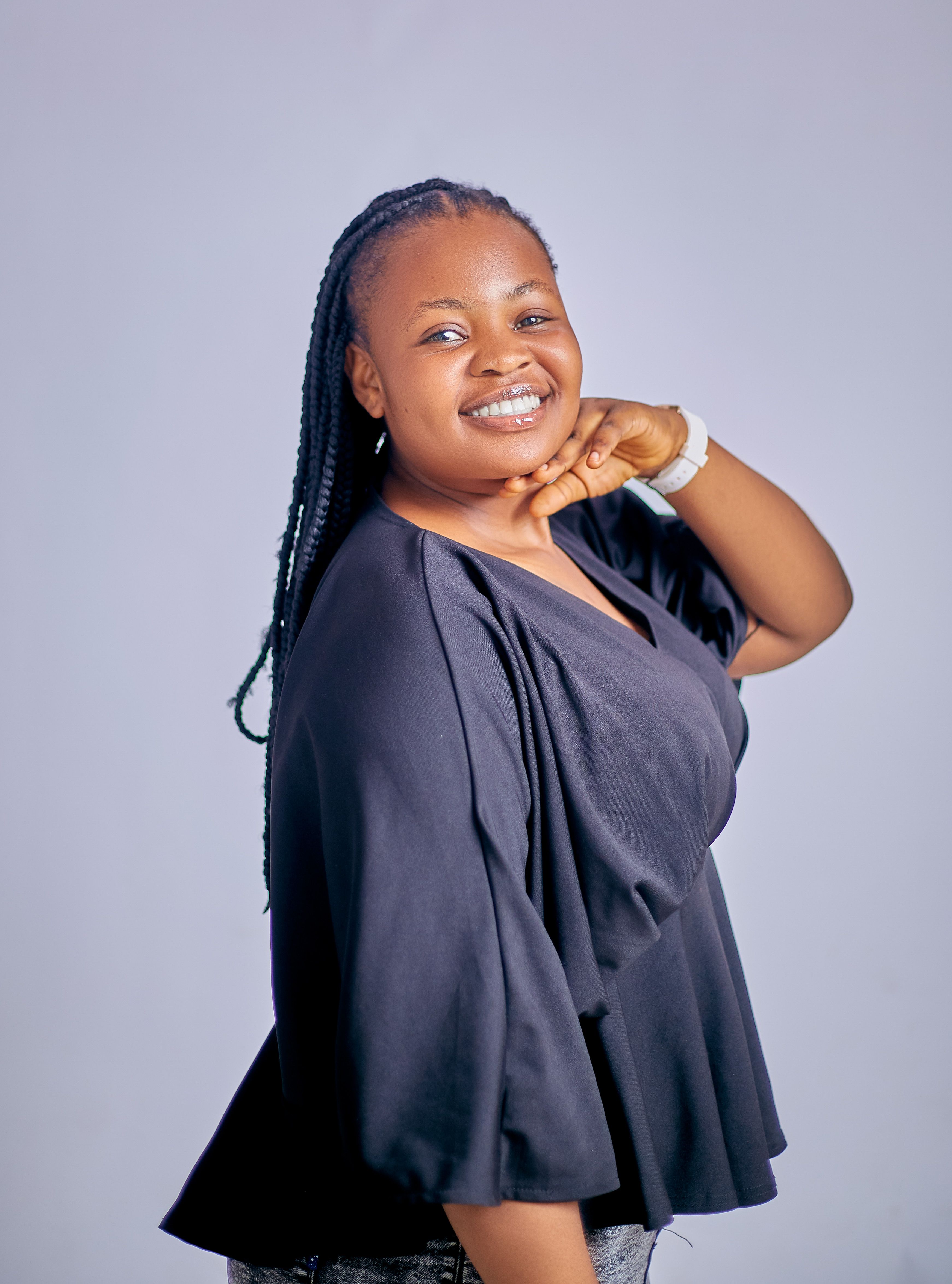 A cheerful woman with braids smiles confidently in a relaxed pose indoors.