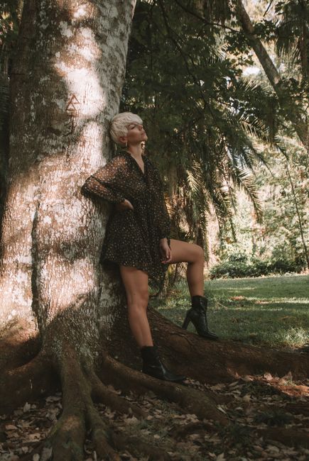 Stylish woman leaning against a tree in a sunlit park, showcasing casual fashion.