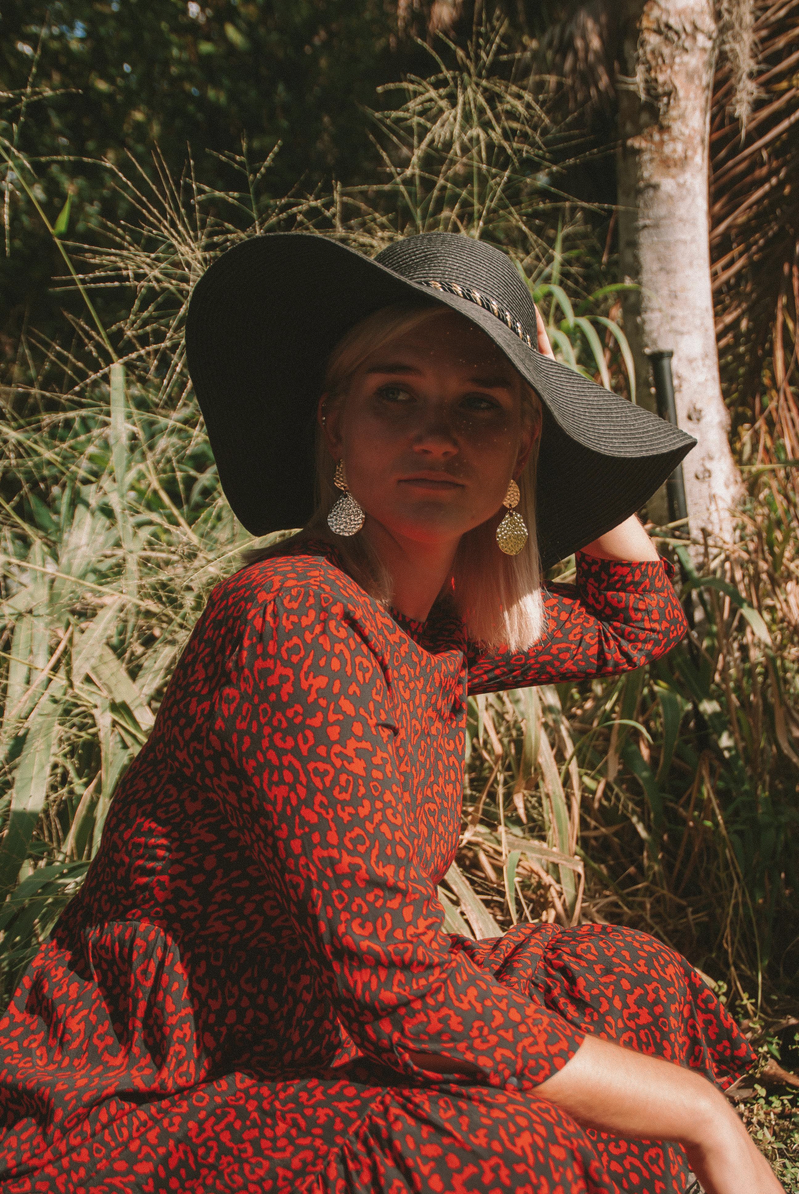 一位时尚女性身着红衣、头戴红帽，在户外自然光下摆姿势