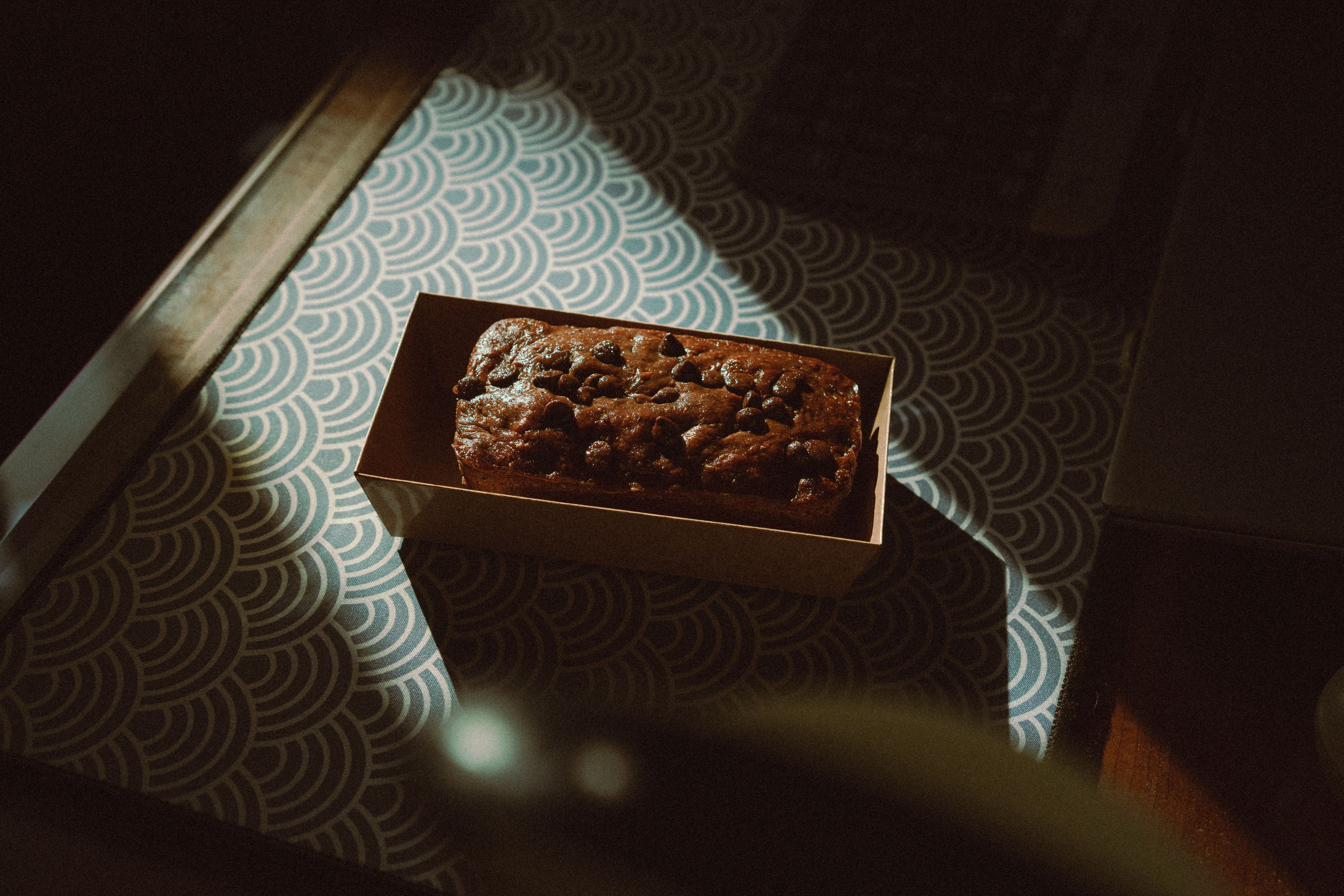 A delectable chocolate cake topped with chocolate chips in a box, captured in warm indoor lighting.