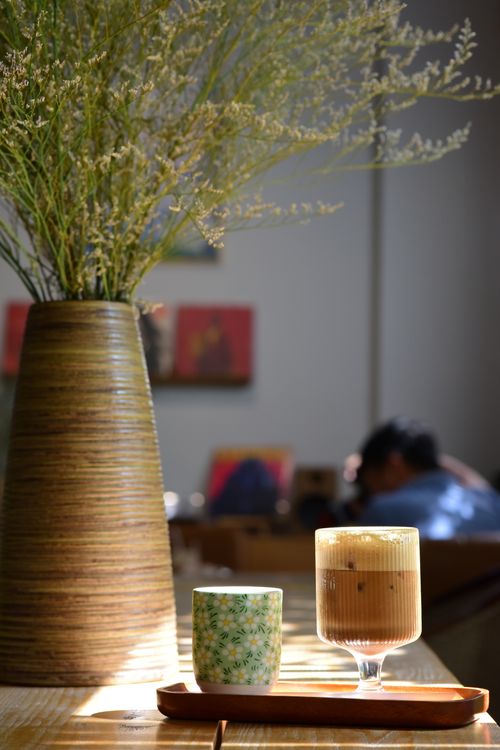Free Warm cafe atmosphere featuring a latte and floral vase on a wooden table, ideal for lifestyle visuals. Stock Photo
