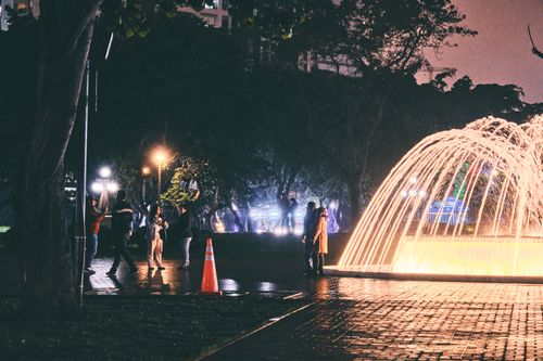Free A beautiful night scene of people near an illuminated park fountain. Stock Photo
