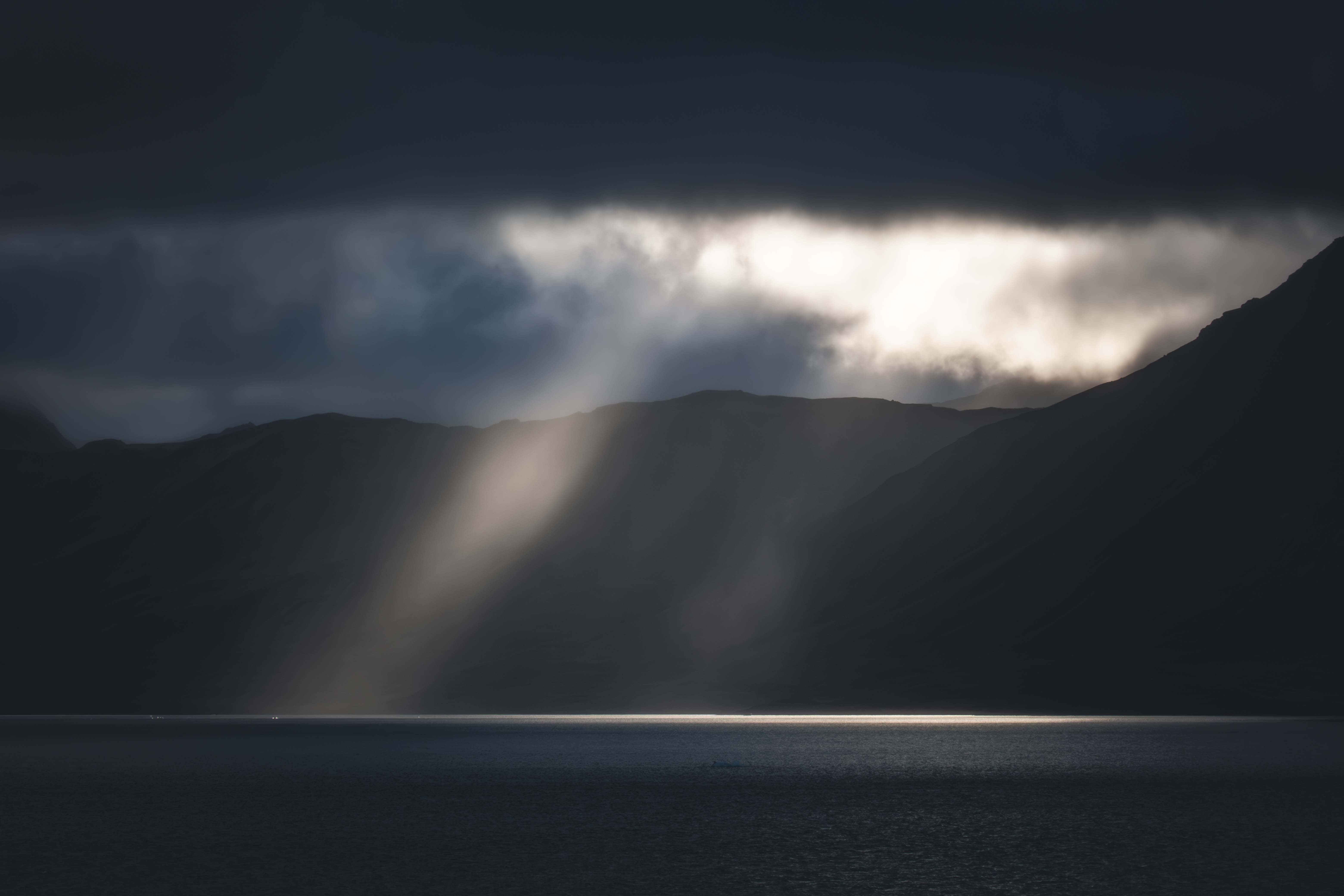 Captivating sunbeam piercing through dark clouds over a serene arctic landscape in Svalbard.