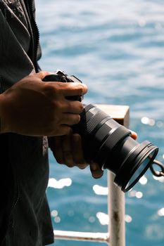Close-up of a photographer holding a camera by the ocean, capturing a serene water view.