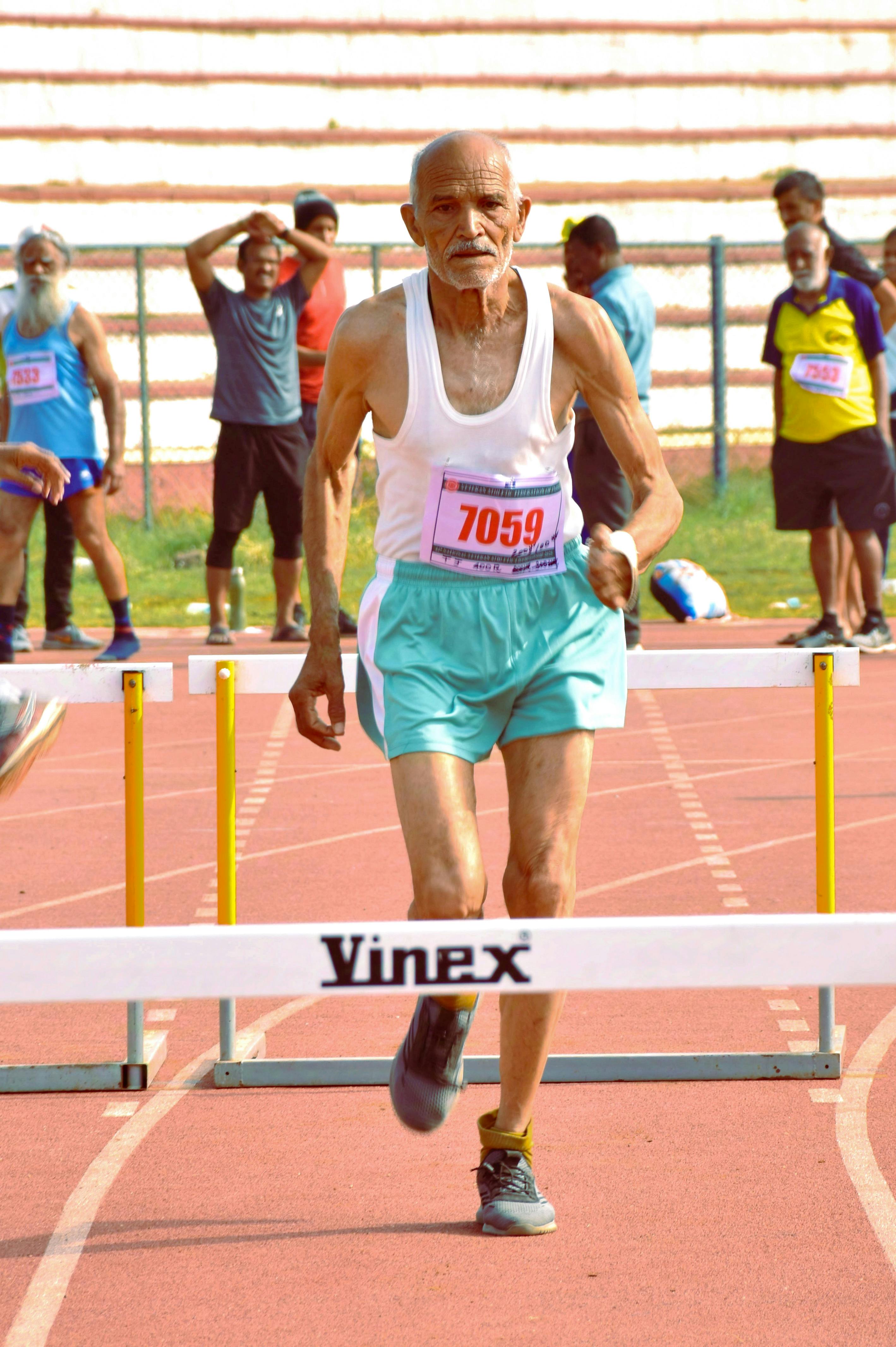A senior athlete competes in a hurdle race showcasing determination and fitness at a sports event.