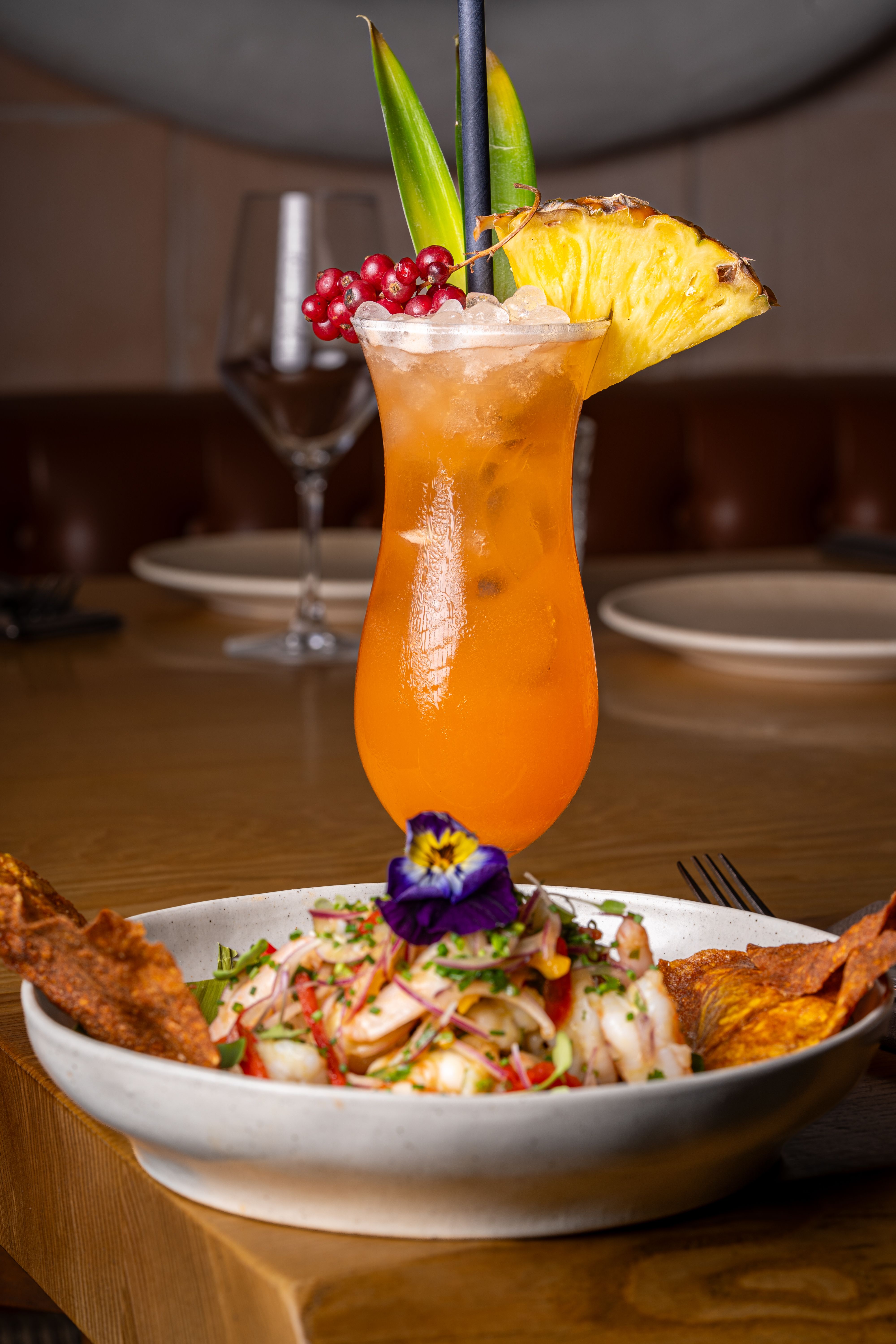 A tall hurricane glass filled with a deep orange-red rum cocktail, garnished with an orange slice and a maraschino cherry on a bar napkin.