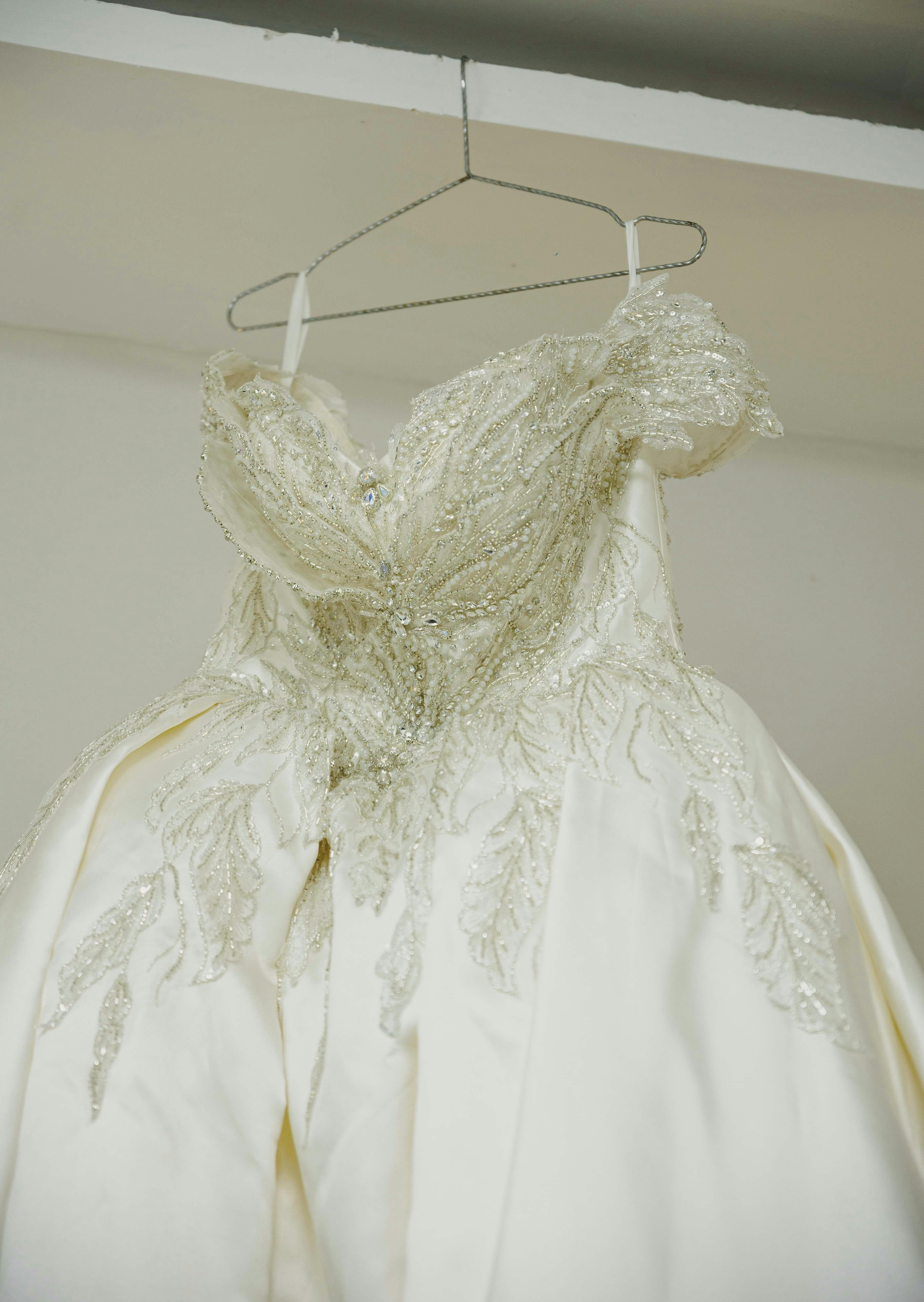 Close-up of a beautiful white wedding gown with intricate lace details hanging on a hanger.