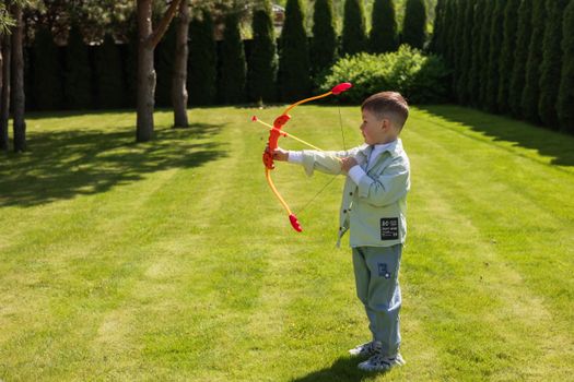 A young boy enjoying a sunny day playing with a toy bow and arrow on a grassy lawn.