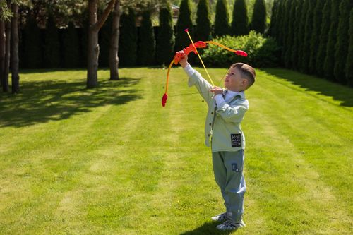 Free Young boy enjoying playtime with a toy bow and arrow in a lush green garden setting. Stock Photo
