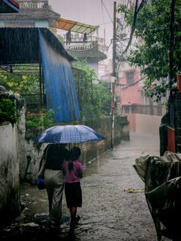 A mother and daughter share an umbrella while walking in a narrow alley during a heavy rainstorm.