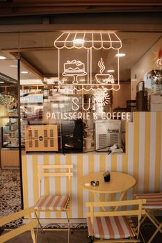 Charming outdoor cafe with a neon sign displaying desserts and coffee on a sunny day.