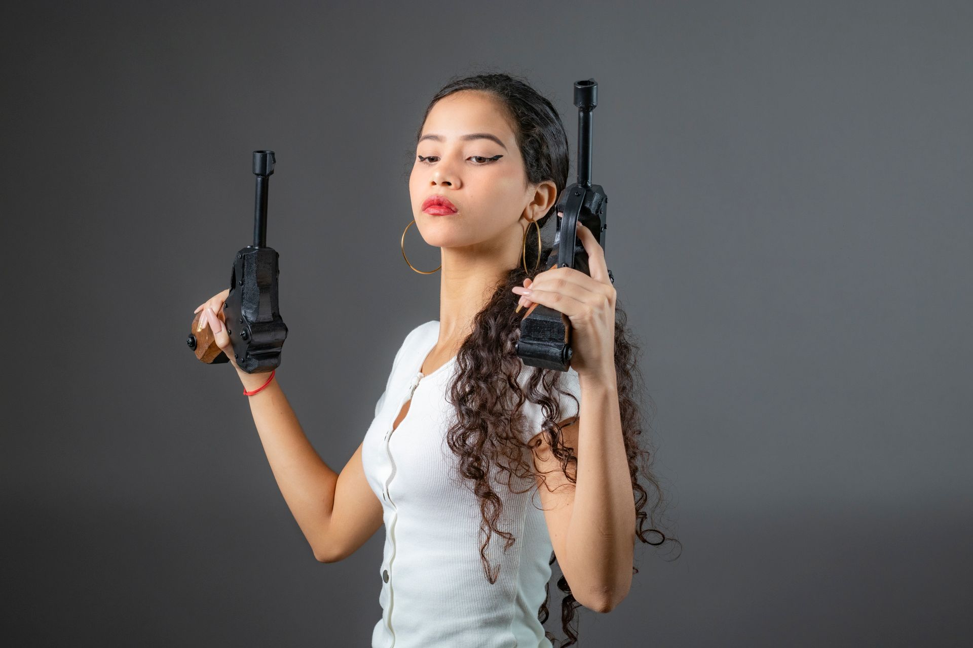 Portrait of a confident woman holding dual vintage movie cameras against a neutral background.