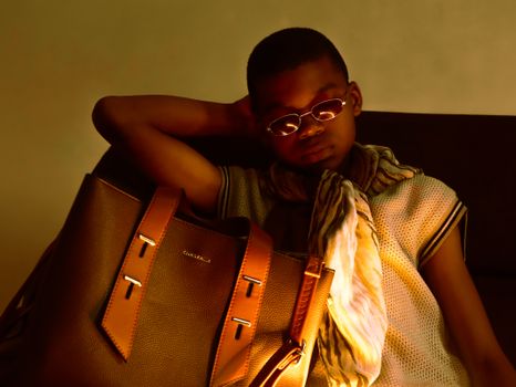 A fashionable teenager poses indoors with a luxury handbag, showcasing high fashion elegance and style.
