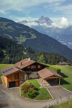 Idyllic wooden chalet with solar panels in the Swiss Alps, set against stunning mountain backdrop.