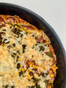 Round homemade pizza with sausage, cheese, corn, and herbs. Perfect for food enthusiasts.