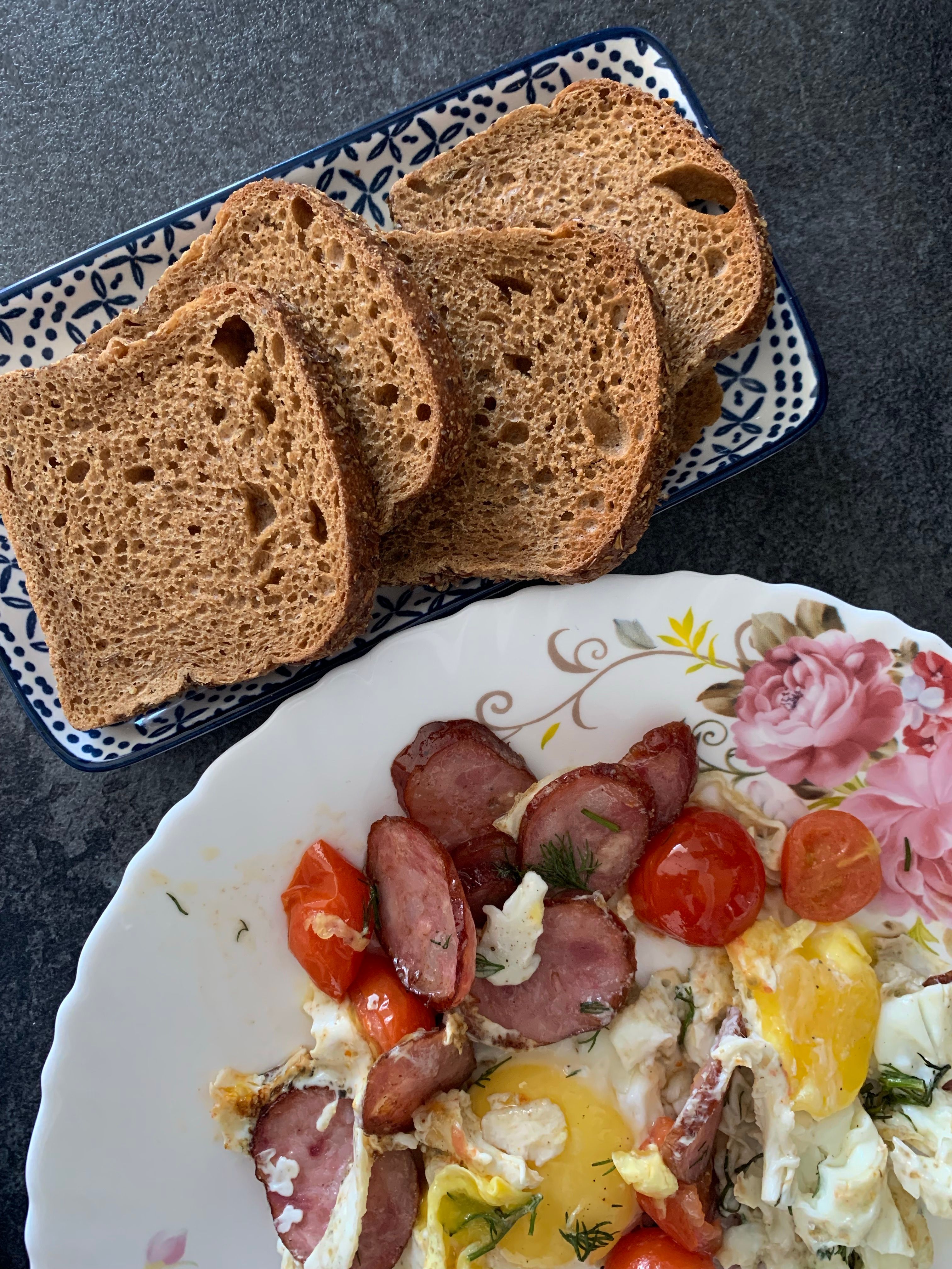 Close-up of a homemade breakfast with sausage, eggs, cherry tomatoes, and sliced bread.