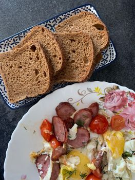 Close-up of a homemade breakfast with sausage, eggs, cherry tomatoes, and sliced bread.