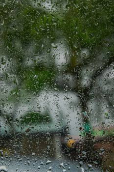 Raindrops on glass blurring the view of green trees outside on a rainy day.