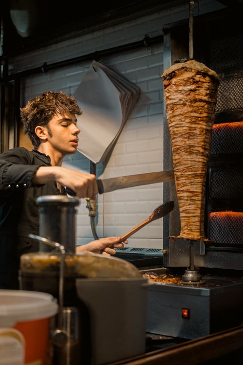 Free A chef skillfully slices a large doner kebab indoors in Istanbul, creating a delicious Turkish meal. Stock Photo