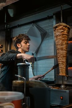 Young male chef expertly slices shawarma in a bustling Istanbul kitchen. Authentic Turkish street food preparation.