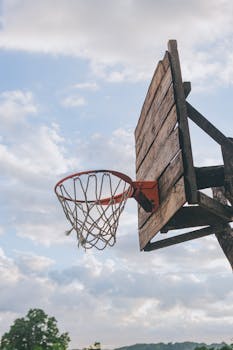 Vintage wooden basketball hoop and net against a cloudy sky backdrop.