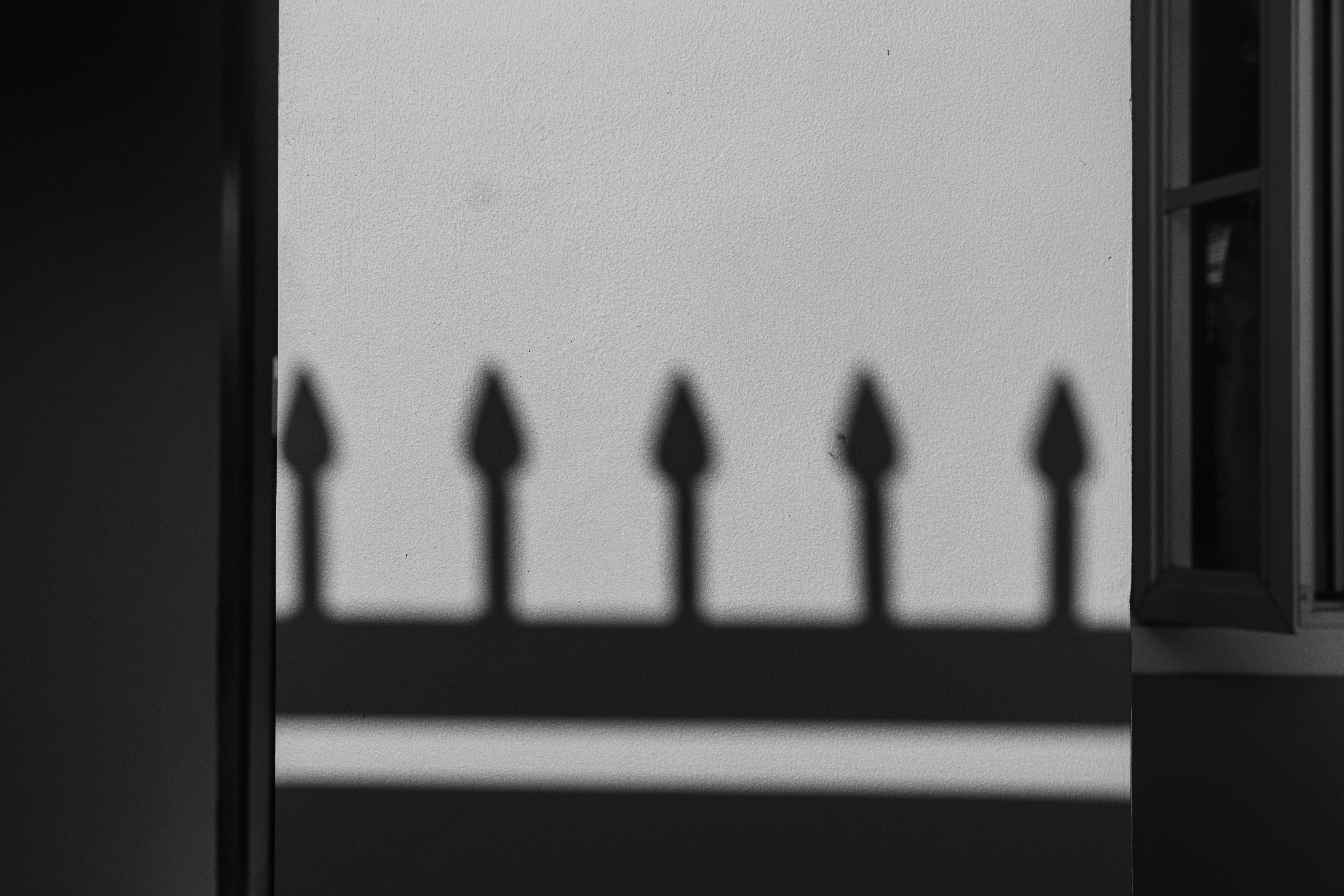 Zadarmo Čiernobiela fotografia tieňov plota vrhaných na stenu, ktoré vytvárajú geometrický vzor. Fotka z fotobanky