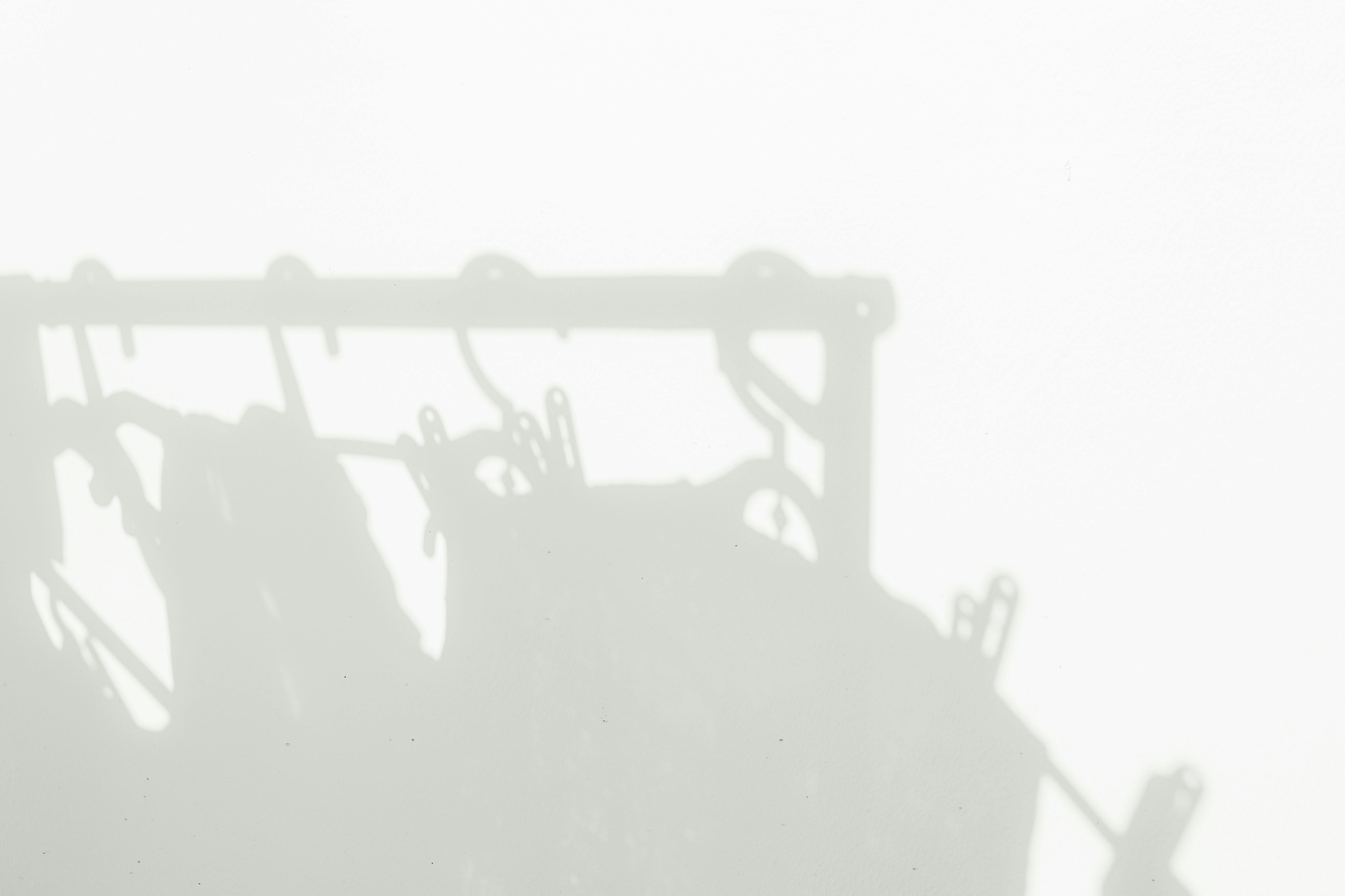 Zadarmo Minimalistický tieň oblečenia a vešiakov na bielej stene, vytvárajúci abstraktné umelecké pozadie. Fotka z fotobanky