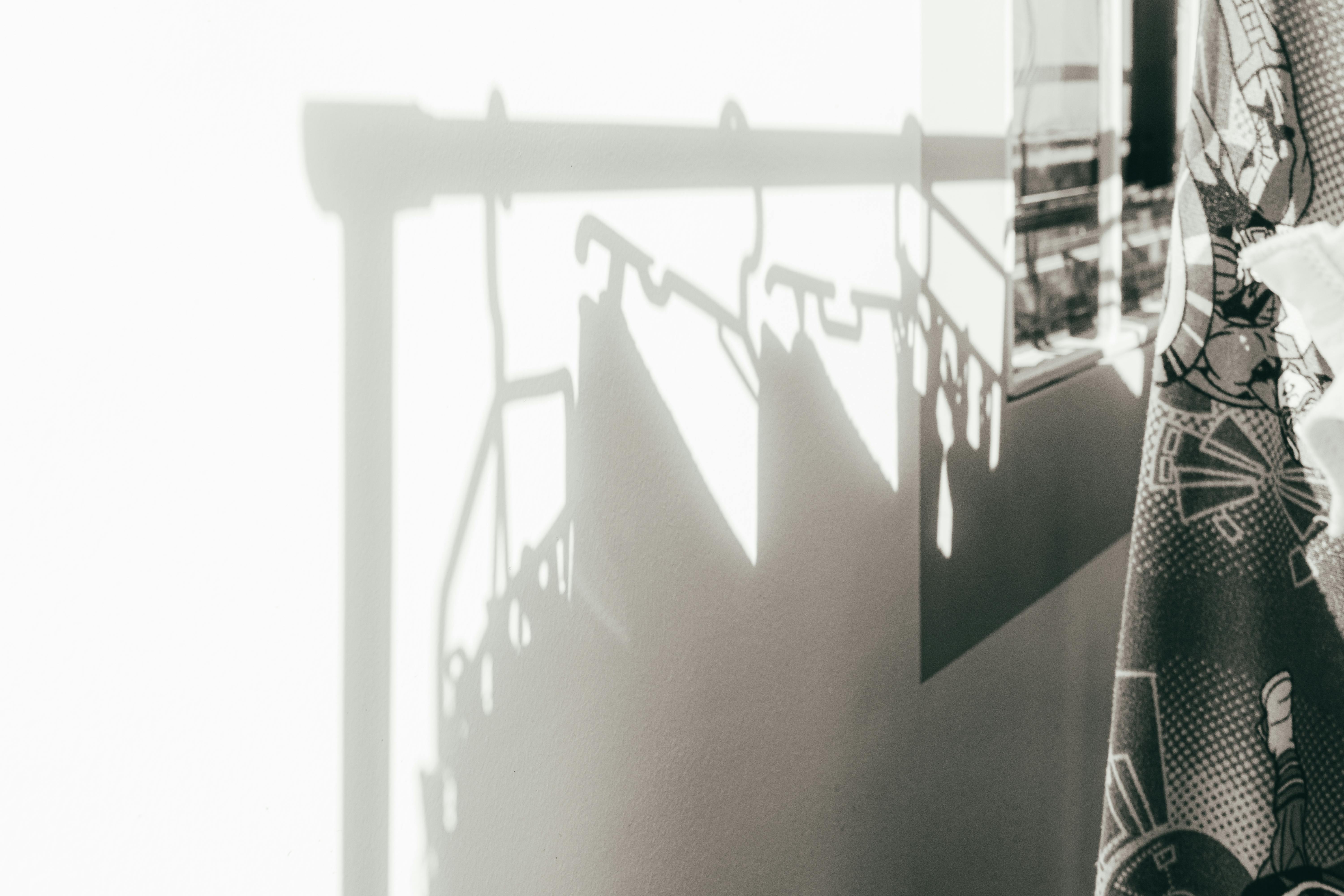 Gratis Composición artística única que captura sombras de perchas en una pared con una cortina estampada. Foto de stock