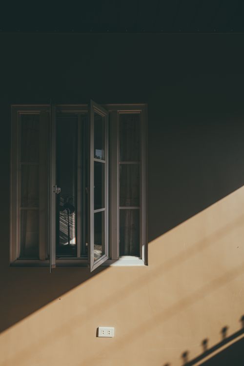 Free A dramatic play of light and shadow on an open window against a dark wall, creating a striking visual effect. Stock Photo
